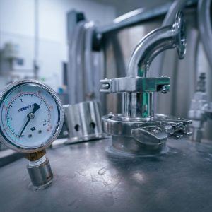 Close-up of a pressure gauge on a stainless steel tank in a sterile industrial setting, showcasing manufacturing technology.